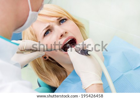 Closeup portrait young female, woman, patient sitting in dentist chair, office with wide open mouth getting oral dental procedure, drilling done by stomatology doctor isolated background clinic office