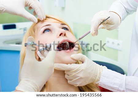 Closeup portrait young female, woman patient sitting in dentist chair, office with wide open mouth getting painful anesthetic injection done by doctor, his assistant isolated background clinic office