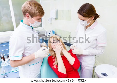 Closeup portrait young terrified girl, woman scared at dentist visit, siting in chair, covering her mouth, doesn\'t want dental procedure, drilling, tooth extraction, isolated clinic office background