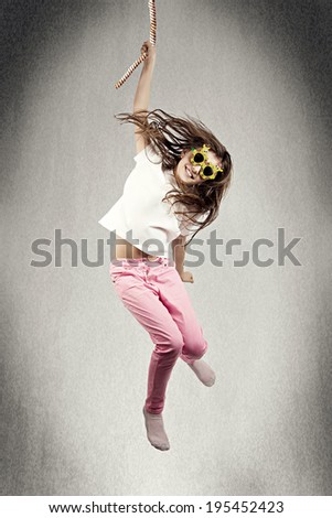 Portrait happy, smiling little girl in sunglasses hanging on rope with one hand, somewhere in space, isolated black background. Human life fate, challenges, destiny, luck, karma, chance concept