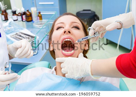 Closeup portrait young female, woman patient sitting in dentist chair, office with wide open mouth getting anesthetic, syringe injection done by doctor, his assistant isolated background clinic office