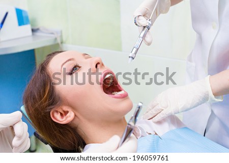 Closeup portrait young female, woman patient sitting in dentist chair, office with wide open mouth getting anesthetic, syringe injection done by doctor, his assistant isolated background clinic office