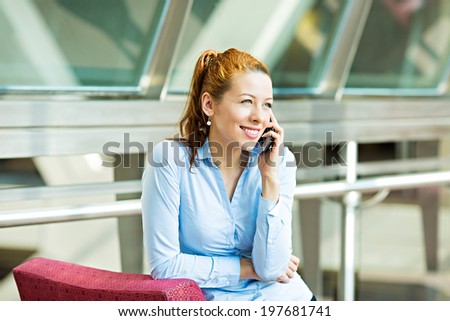 Closeup portrait businesswoman talking on mobile phone. Businesswoman on cellphone sitting in hall corporate office talking on smart phone. Happy smiling employee isolated background building windows
