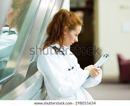 Closeup portrait, young confident, thoughtful female doctor, healthcare professional reading patient chart isolated background hospital hallway. Patient visit health care, management, plan, diagnosis