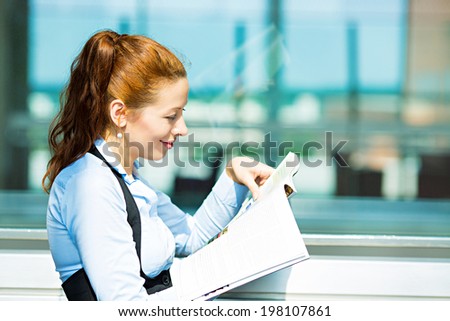 Closeup side view portrait business woman reading latest news in magazine, smiling happy, great stock market news isolated background corporate office windows. Positive human facial expression emotion