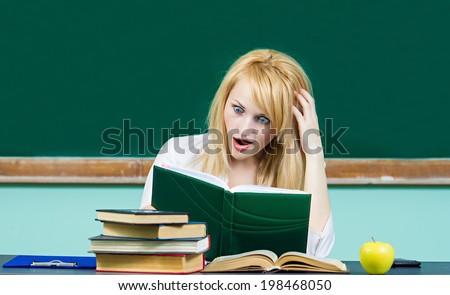 Closeup portrait shocked, surprised overwhelmed student sitting at desk in front pile books, studying preparing finals can\'t believe her eyes isolated chalkboard background. Education. Face expression