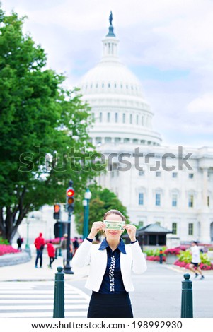 Closeup portrait quiet corrupt politician in washington dc, woman holding covering her eyes with dollar bills isolated Capitol building background. Human nature, life perception Greed politics concept