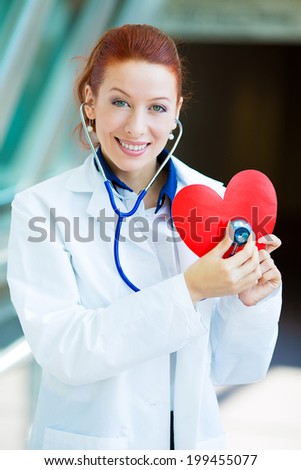 Closeup portrait smiling cheerful health care professional, pharmacist, dentist, nurse cardiologist doctor with stethoscope, holding listening heart isolated background hospital hallway. Patient visit