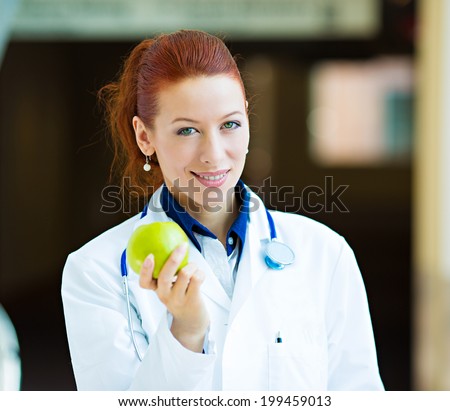 Closeup portrait smiling happy health care professional, doctor, nurse in lab coat offering green apple, isolated background hospital hallway. A day keeps doctor away concept. Nutrition, healthy diet