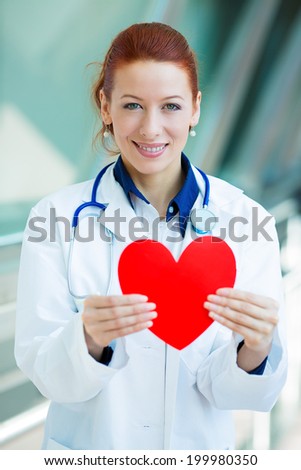 Closeup portrait happy smiling female health care professional, woman family doctor cardiologist, nurse with stethoscope holding red heart, isolated hospital hallway background. Patient plan, visit