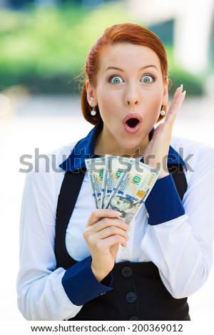 Closeup portrait, super happy excited, surprised successful young business woman holding money dollar bills in hand, isolated background street building. Financial reward. Facial expression, emotions