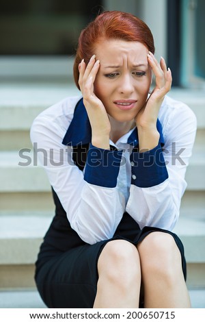 Closeup portrait unhappy business woman, head on hand sitting on stairs, bothered by mistake, having bad headache isolated background corporate office windows. Negative human emotion facial expression