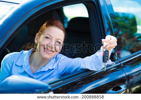 Closeup portrait happy, smiling, young, attractive woman, buyer sitting in her new black car showing keys isolated city street dealership lot background. Personal transportation, auto purchase concept