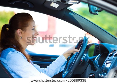 Portrait smiling, attractive brunette woman, buckled up, driving, testing her new black car, automobile, purchased at dealership, isolated street, city traffic background. Safe driving habits concept