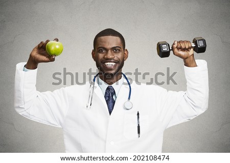 Closeup portrait happy, smiling male health care professional, doctor in lab coat holding, lifting green apple, dumbbell, promoting, advising on healthy life style, isolated grey, black background
