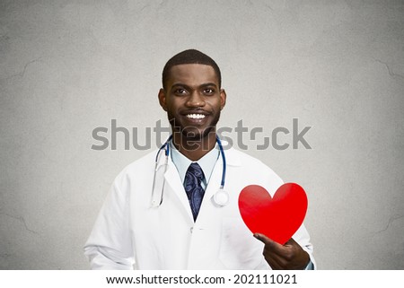 Closeup portrait happy, smiling male health care professional, man family doctor, cardiologist with stethoscope holding red heart, isolated black, grey background. Patient plan, cardiovascular system