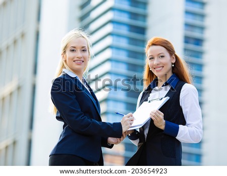Closeup portrait two smiling young business women, company employees signing contract document, agreement paper, paperwork isolated corporate office background.