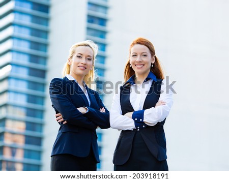 Closeup portrait two young beautiful, happy business women, employees smiling isolated urban, city building background on sunny day. Positive human emotion, facial expression attitude, life perception