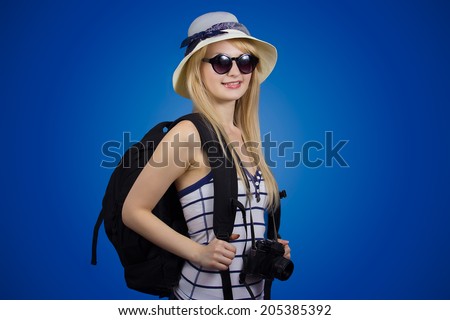 Closeup portrait happy, smiling girl, young woman with pack bag, photo camera, hat, sunglasses  going on journey isolated blue background. Positive human emotions, facial expressions, life perception