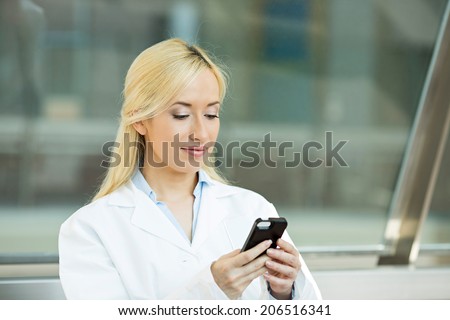 Closeup portrait young healthcare professional, doctor, nurse, dentist, researcher, physician assistant reading text sms, message on cellphone holding smart phone isolated hospital hallway background