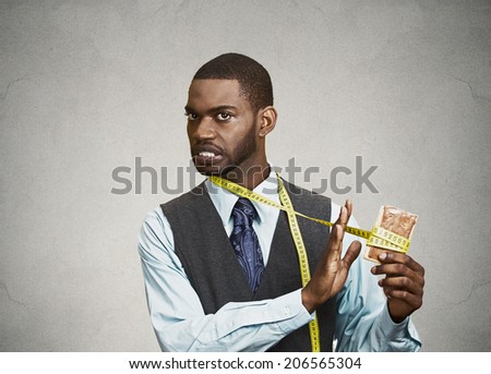 Closeup portrait funny young, confused man holding fatty, sweet cookie with measuring tape around, trying to withstand resist, avoid temptation to eat it isolated black background. Face expressions