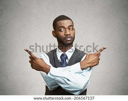Closeup portrait confused young business man pointing in two different directions, not sure which way to go life, hesitant to make decision isolate black background. Emotion, facial expression feeling