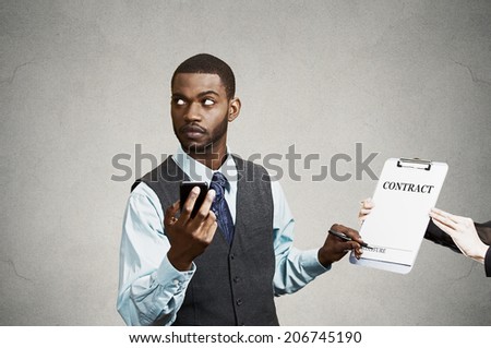 Closeup portrait annoyed skeptical sneaky businessman signing contract without looking at document, corporate executive holding mobile smart phone isolated grey black background. Human face expression