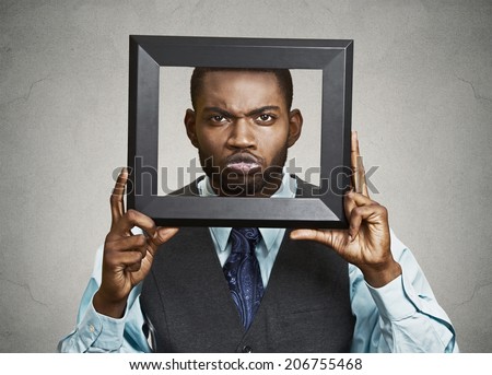 Closeup portrait businessman executive looking curious surprised confused skeptical through black picture frame thinking beyond borders accepted rules isolated grey background. Face expression emotion