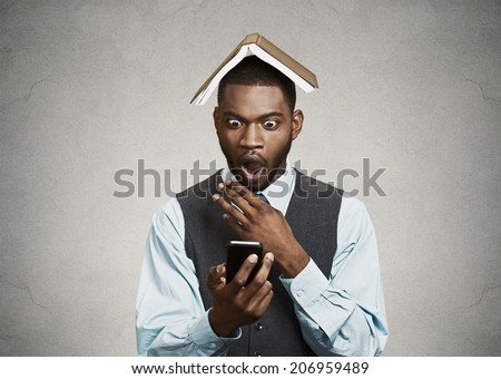 Closeup portrait surprised business man, executive reading, browsing news on smart phone holding mobile, book over head isolated black background. Human face expression, emotion, corporate lifestyle