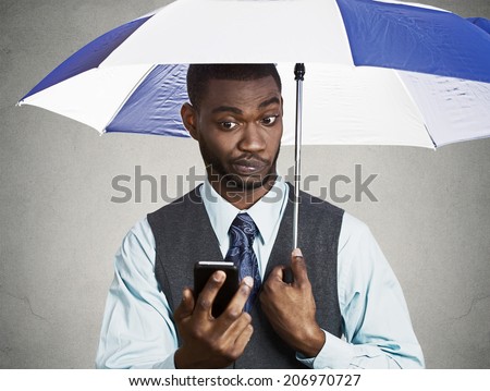 Closeup portrait skeptical confused corporate business man reading breaking news on smart phone holding umbrella rainy day, protected from rain isolated black background. Human face expression emotion