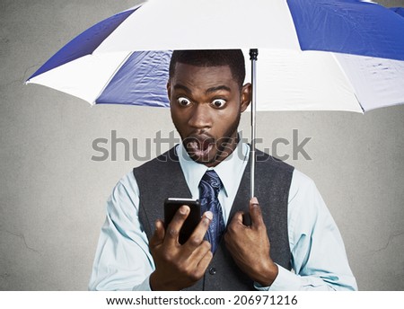 Closeup portrait shocked, surprised business man, corporate executive reading bad, breaking news on smart phone holding umbrella protected from rain isolated black background. Face expression, emotion
