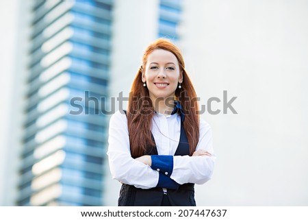 Closeup portrait young, attractive, confident business woman, company executive employee standing with arms crossed isolated in front of corporate office building. Positive face expressions, emotions