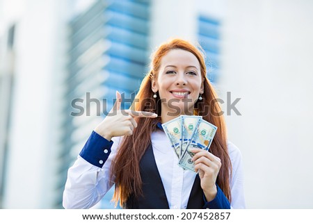 Closeup portrait super happy excited successful young business woman holding money dollar bills in hand isolated corporate office background. Positive emotion face expression feeling. Financial reward