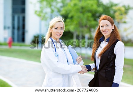 Closeup portrait happy, smiling health care professional, doctor, nurse shaking hands with satisfied female patient, isolated outdoors hospital background. Clinic care coverage, treatment plan concept