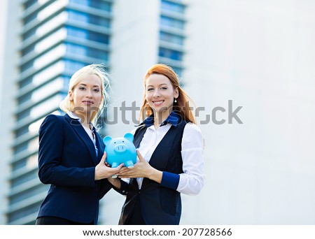 Closeup portrait two smiling business women bank employee, customer holding piggy bank depositing money isolated corporate office background. Financial saving banking concept. Positive face expression