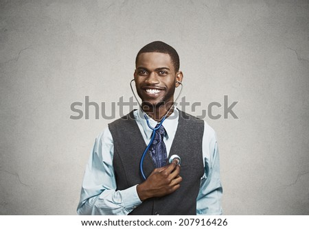 Closeup portrait smiling executive man, business person, worker listening to his heart with stethoscope isolated grey background. Preventive medicine, financial condition concept. Face expressions