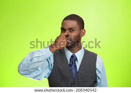 Closeup portrait young executive man, disgust on face, pinches his nose, something stinks, bad smell, situation isolated green background. Negative emotion facial expression, perception body language