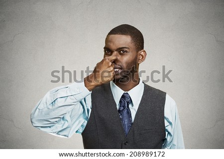 Closeup portrait young executive man, disgust on face, pinches his nose, something stinks, bad smell, situation isolated grey background. Negative emotion facial expression, perception body language