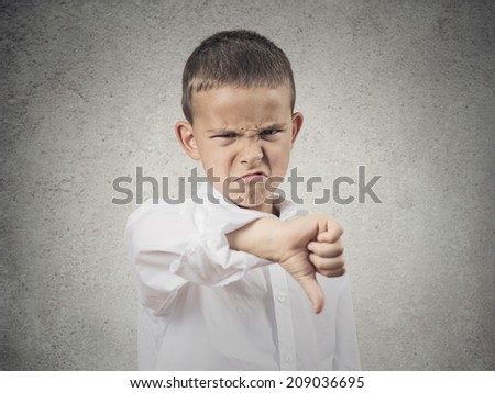 Portrait unhappy, Angry, Displeased Child giving Thumbs Down hand gesture, isolated grey wall background. Negative human Face Expressions, Emotions, Feelings, attitude, life perception, body language