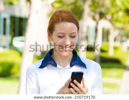 Closeup portrait happy, cheerful, girl, excited by what she sees on cell phone isolated outdoor background corporate office. Facial expression reaction. Business woman sending text message from mobile