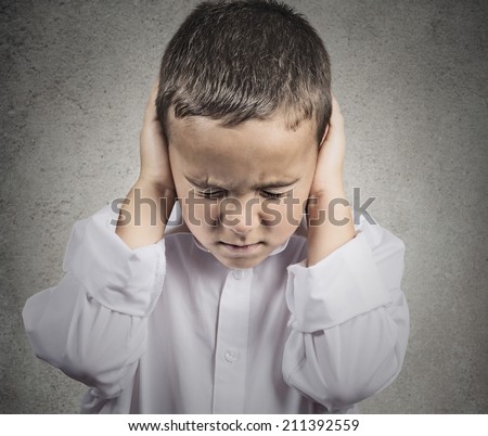 Closeup portrait, headshot child, boy covering ears with hands, doesn\'t want to hear loud noise, conversation isolated grey wall background. Human face expression, emotion, feeling reaction perception