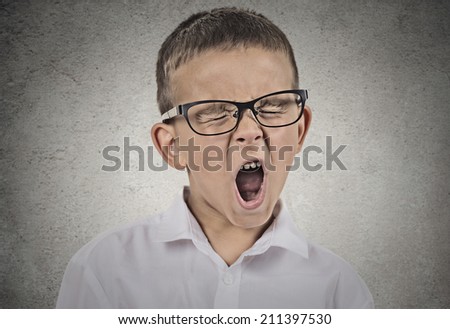Closeup portrait tired child with glasses yawning, isolated on grey wall background. Human facial expressions, emotions, feelings, body language. Long school hours, busy day concept.