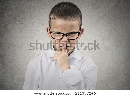 Closeup portrait young angry child, boy placing finger on lips as if to say, shhh, be quiet, silence, isolated grey wall background. Facial expression, human emotions, signs, symbols, body language