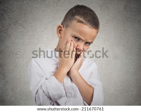 Closeup portrait sad, depressed, alone, unhappy, gloomy child boy resting his face on hands, isolated grey wall background. Negative human emotion face expression feeling life perception body language