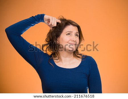 Closeup portrait young woman scratching head, thinking daydreaming deeply about something, looking up isolated orange background. Human facial expression, emotion, feeling, signs symbol, body language