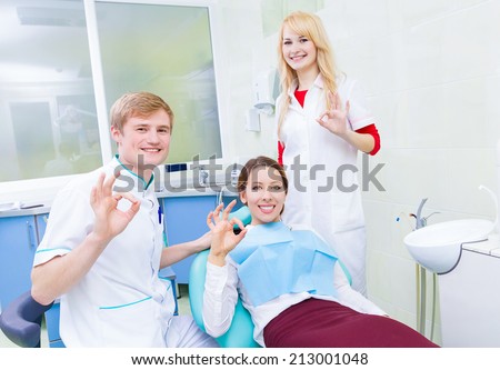 Group portrait happy health care professionals dentist assistant satisfied smiling female patient in medical office giving ok sign. Clinical patient plan care excellence concept. Body language gesture
