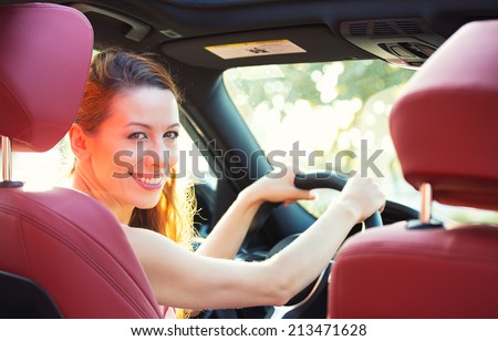 Portrait happy woman in new car, indoor keeps wheel, turning around, smiling looking at, talking to passengers sitting in back seat asks right directions to drive. Driver license exam, test concept