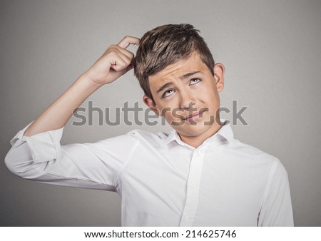 Closeup portrait young man scratching head, thinking daydreaming deeply about something, looking up, isolated grey wall background. Human facial expression, emotion, feeling, sign symbol body language