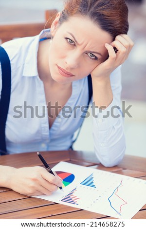 Closeup portrait unhappy business woman looking displeased working on financial report stockholder meeting siting at table documents, writing, distressed, isolated outside. Negative expression emotion