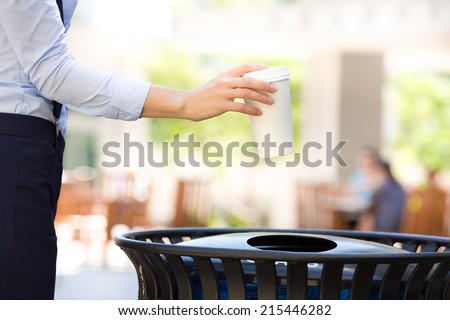 Closeup cropped image woman\'s hand throwing empty paper coffee cup in recycling bin, isolated outside, trees background. Recycling, eco friendly approach concept. Keep streets, city, earth clean